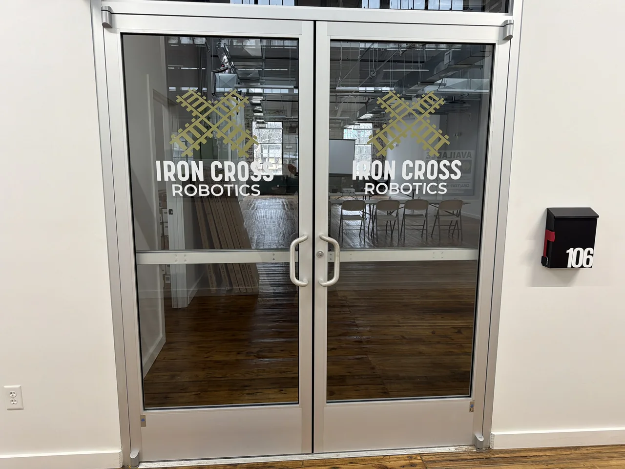 The Iron Cross Robotics entrance — glass double doors bearing the logo at Suite 106 in the Virginia Metalcrafters Building