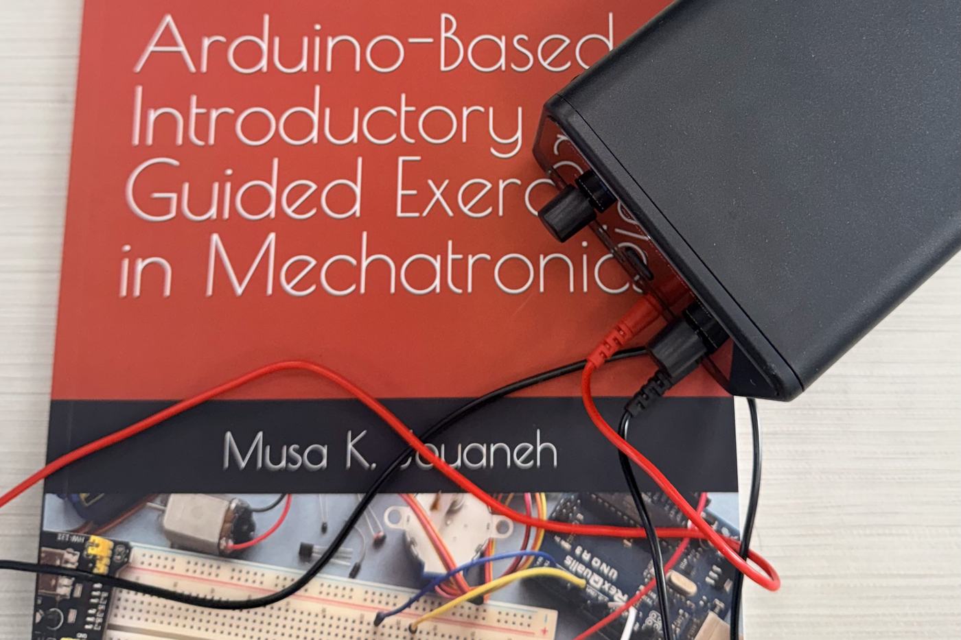 A mechatronics textbook on the bench beside a breadboard wired to an Arduino and a bench power supply