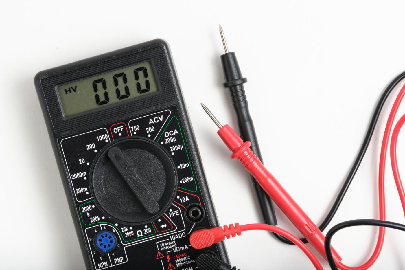 A digital multimeter with test leads on a bench