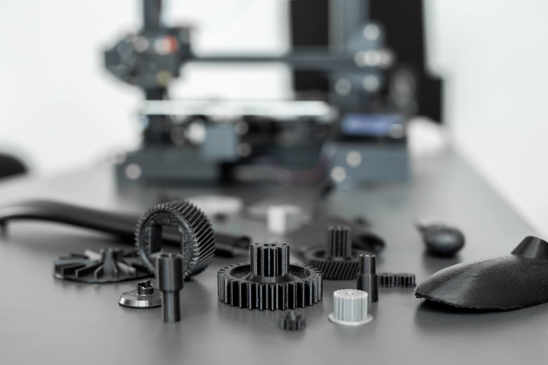 3D-printed gears and parts on a bench beside a printer